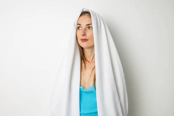 stock image Young woman covering her head with a white sheet on a white background.