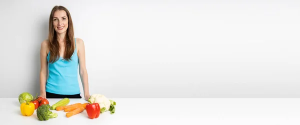 キッチンの新鮮な野菜で笑顔の若い女性がテーブルの上にあります バナー — ストック写真