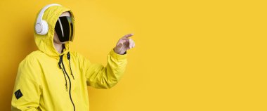 Siber punk gözlüklü, kulaklıklı genç bir kadın sarı arka planda sanal ekrana tıklıyor..