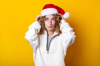 Sarı arka planda Noel Baba şapkası takan kıvırcık bir genç kadın.