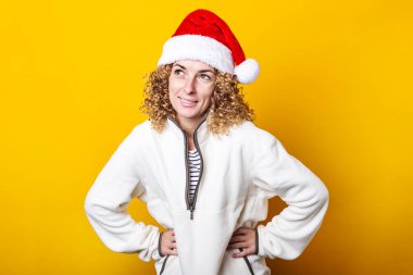 Sarı arka planda, Noel Baba şapkalı, gülümseyen kıvırcık kadın.
