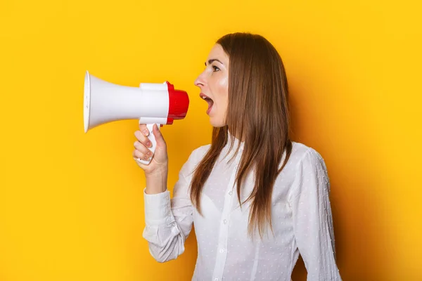Young woman in a white shirt shouts into a megaphone on a yellow background. Concept for hiring, listing, help wanted. Banner.