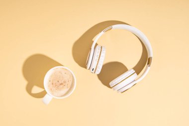 Kapuçino, bej arka planda kablosuz kulaklık. Düz yatış, üst görünüm 