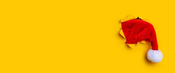 stock image Santa Claus hat in a hole in a torn yellow background. Banner.