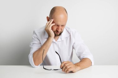 Genç adam masada otururken ağırlığı tutarak gözlüklerini çıkarıyor..