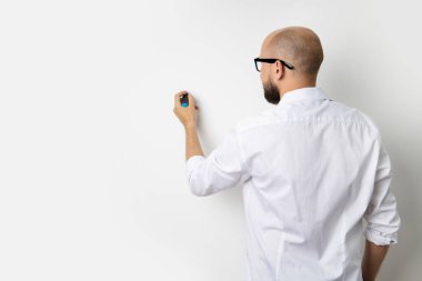 Genç adam tahtaya bir kalemle yazı yazarken arkası dönük duruyor..