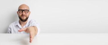 Gülümseyen genç adam beyaz arka planda masada otururken selamlaşmak için elini uzatıyor. Pankart.