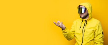 Young man in cyberpunk glasses clicking on an invisible screen on a yellow background. Banner.