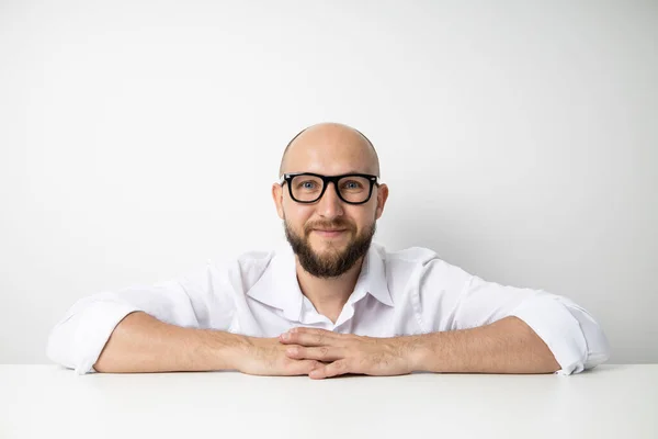 stock image Smiling young man with his hands clasped while sitting at the table on a white background.