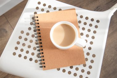 Beyaz bardakta kahve, beyaz sandalyede defter. Üst görünüm düzlüğü 