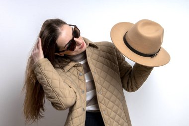 Ceketli gülümseyen genç kadın beyaz bir duvarın arkasında şapkasını çıkardı. 