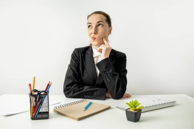 Thoughtful young woman in jacket sitting at table at workplace.