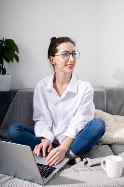 Kanepede oturan dizüstü bilgisayarlı gülümseyen genç kadın.