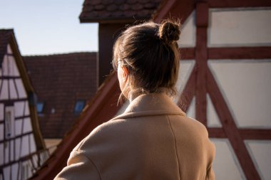 Sırtı evlerin arka planında duran ceketli genç bir kadın..