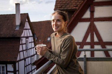 Terasta bir fincan kahveyle gülümseyen genç bayan..