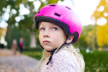 Sad child girl in a pink helmet in the park.