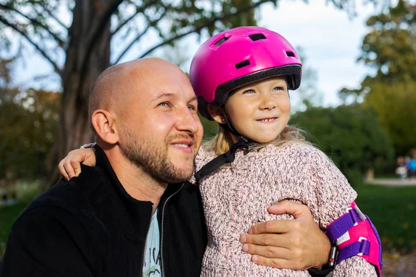 Smiling dad and little daughter in a helmet look at the sky.