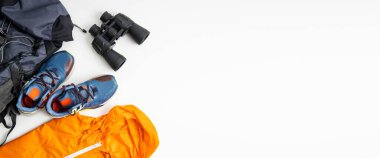 Dürbün, turist çantası, yağmurluk, beyaz arka planda ayakkabılar. Üst manzara, düz yatış. Pankart.