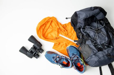 Binoculars, tourist backpack, raincoat, shoes on a white background. Top view, flat lay.
