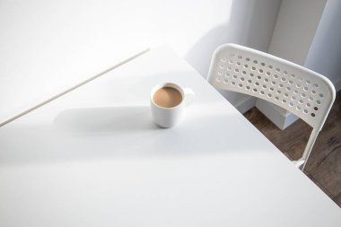 Beyaz bardak beyaz bir masada, doğal ışık altında. Üst görünüm düzlüğü 