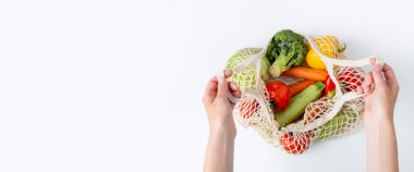 Female hands take out fresh vegetables from a bag on a white background. Top view, flat lay. Banner.