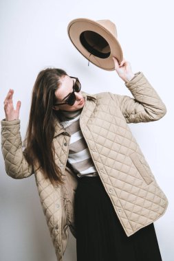 A young woman in a jacket took off her hat near a white wall