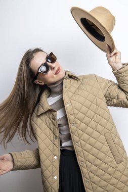 A young woman in a jacket took off her hat near a white wall