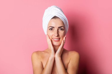 Kafasında havlu olan gülümseyen genç bir kadın, pembe arka planda çıplak omuzlar. 