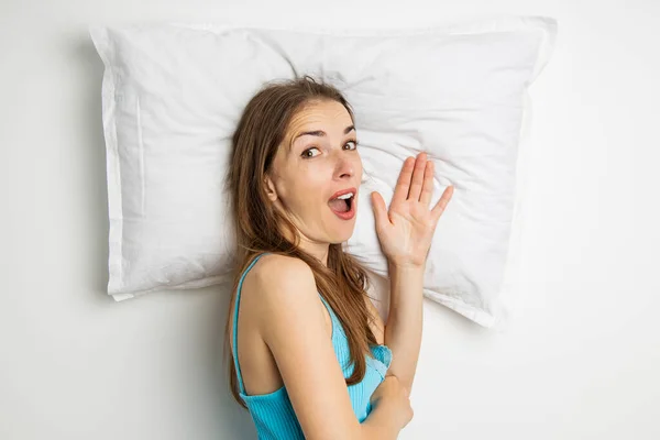 Surprised young woman lying on a pillow on a white background. Top view, flat lay.