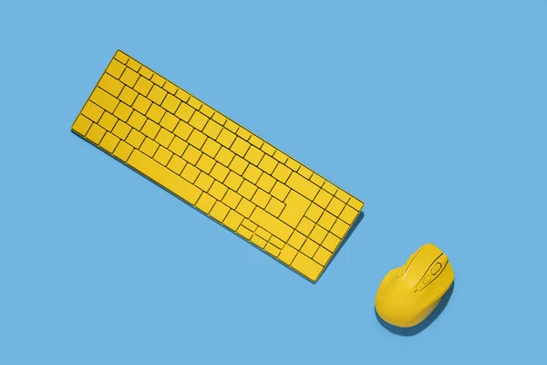 Yellow keyboard and yellow computer mouse on a blue background. Top view, flat lay.