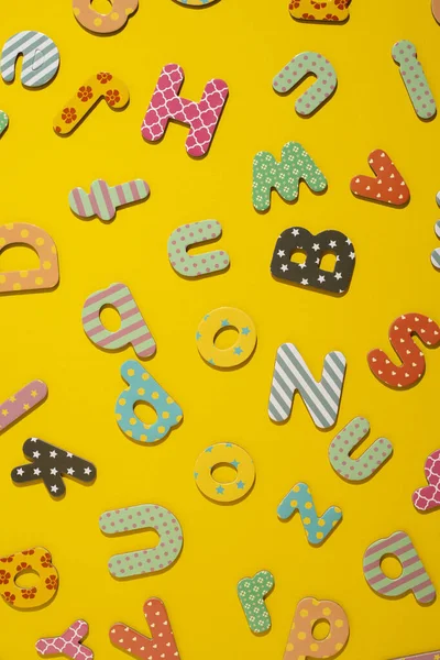 Many multi-colored letters of the alphabet on a yellow background. Top view, flat lay.