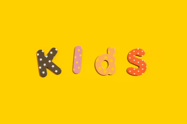 stock image The word kids from multi-colored letters of the alphabet on a yellow background. Top view, flat lay.