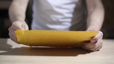 Adam zarfı açar ve mektubu okur. Sadece eller görünür.