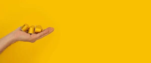 Coffee capsules in the female palm on a yellow background. Banner.