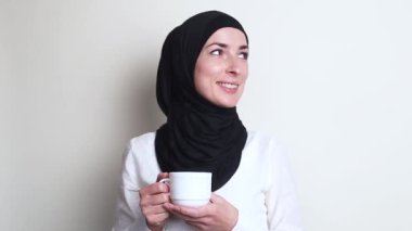 Elinde kupa tutan tesettürlü genç bir kadın.