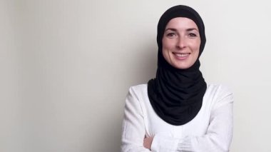 Beyaz arka planda gülümseyen tesettürlü genç kadın.