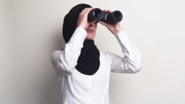 Beyaz arkaplanda dürbünle bakan tesettürlü genç kadın