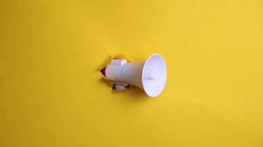 Megafon sarı arka planda bir delikten dışarı bakıyor.