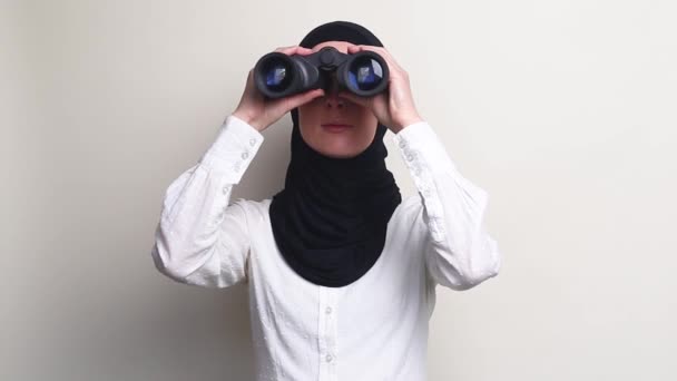 头戴头巾的年轻女子从双筒望远镜看白色背景 — 图库视频影像