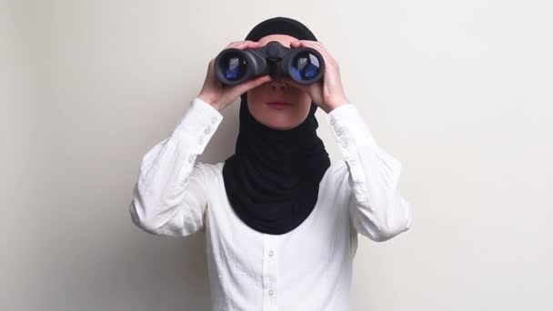 头戴头巾的年轻女子从双筒望远镜看白色背景 — 图库视频影像