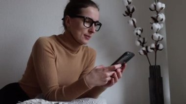 Odada telefonu olan gözlüklü genç bir kadın..