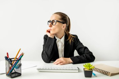 Pensive businesswoman in a jacket in glasses with a keyboard sitting at the workplace.