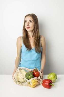 Gülümseyen genç kadın beyaz arka plana sebze koyuyor..