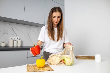 Mutfaktaki bir torbada sebze toplayan genç bir kadın..