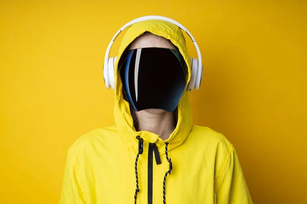 Young woman in cyberpunk glasses with headphones in a yellow jacket on a yellow background.