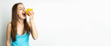 Genç bir kadın, beyaz arka planda taze sarı biber yerken gözlerini bozdu. Pankart.