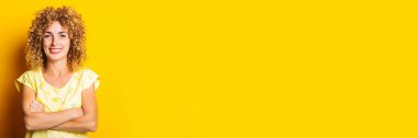 Sarı arka planda çapraz kollu güzel kıvırcık kadın. Pankart