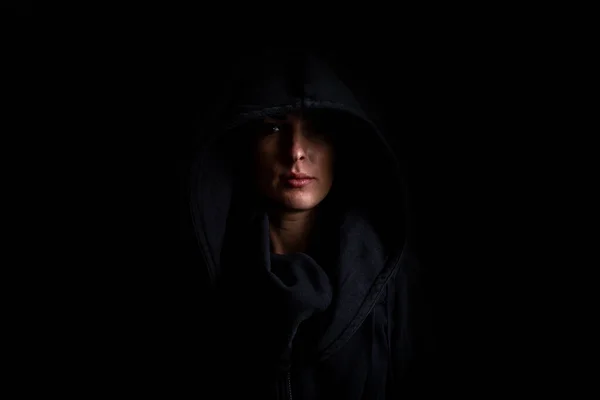 Young woman in a black hood on a black background.