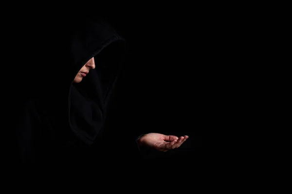 Young woman in a black hood with outstretched hand on a dark black background