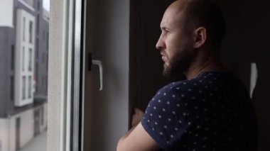 Genç adam pencereden dışarı bakıyor ve pencerenin kepenğini kapatıyor..